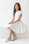Vestido Rumi blanco, niña sentada en un banco blanco, vista frontal