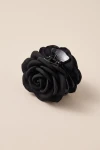 Pinza cangrejo negra con flor de tela sobre fondo beige, vista de tres cuartos