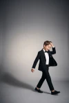 Traje Sam negro para niño en movimiento sobre fondo gris, americana abierta, cuerpo entero